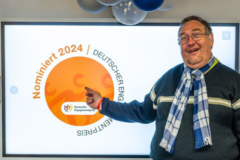 Christian Specht steht vor einem Whiteboard und zeigt auf das Logo Deutscher Engagementpreis, Nominiert 2024